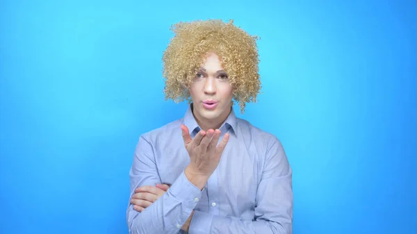 Hombre con maquillaje y una peluca sobre un fondo azul envía un beso —  Fotos de Stock