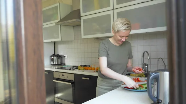 Nainen leikkaa vihanneksia välipala keittiössä kotona — kuvapankkivalokuva