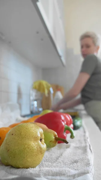 Tiro vertical, uma mulher lava legumes e frutas na cozinha em casa . — Fotografia de Stock