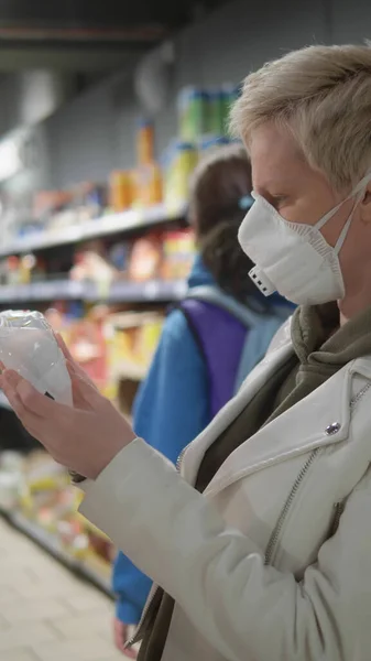 Pionowy strzał. Blondynka w masce medycznej w spożywczaku. pandemia — Zdjęcie stockowe