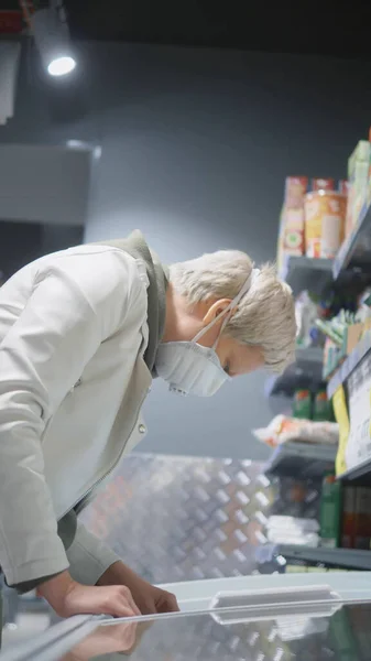Disparo vertical. Mujer rubia con máscara médica en la tienda de comestibles. pandemia — Foto de Stock