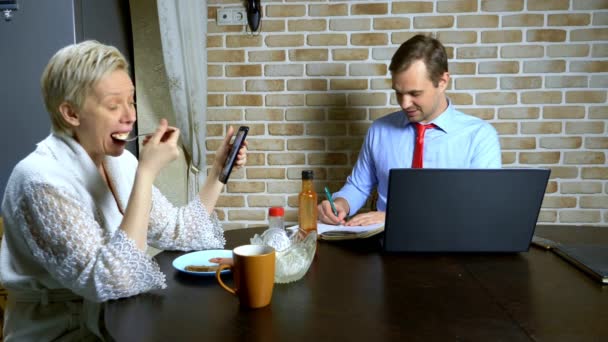 一个男人在家里用笔记本电脑在厨房里干活，妻子在吃饭 — 图库视频影像