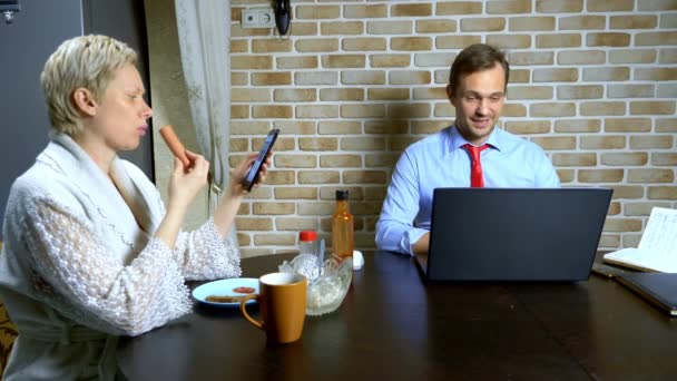 Um homem que trabalha em casa no laptop na cozinha, esposa come — Vídeo de Stock