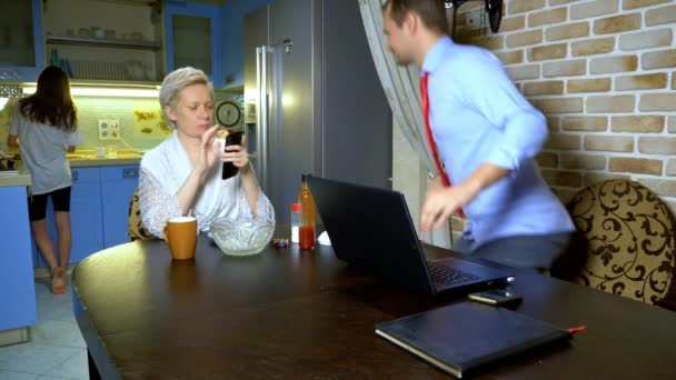 Evde çalışan bir adam mutfaktaki dizüstü bilgisayarda çalışıyor, karısı yemek yiyor. — Stok video