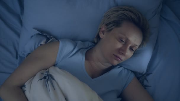 Een vrouw die lijdt aan slapeloosheid ligt in bed in het donker met haar ogen open. — Stockvideo