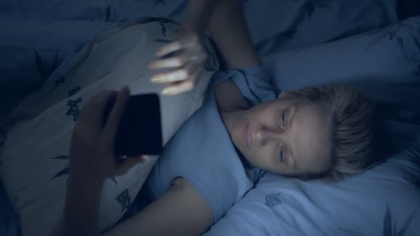 Verticalmente. mujer que sufre de insomnio utiliza un teléfono inteligente mientras está acostada en la cama — Vídeos de Stock