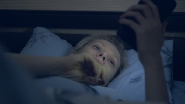 Wanita yang menderita insomnia menggunakan smartphone saat berbaring di tempat tidur dalam gelap — Stok Video