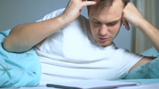 Un hombre escribe en documentos de papel acostado en la cama. trabajo en casa . — Vídeo de stock