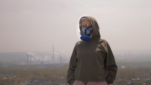 Una mujer en un respirador se para en el fondo de las pipas de la fábrica de fumar — Vídeos de Stock