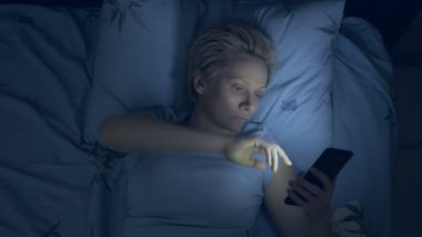 Uykusuzluk çeken kadın karanlıkta yatarken akıllı telefon kullanıyor.