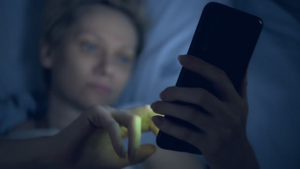 Nő szenved álmatlanságban használ egy okostelefon, miközben fekszik az ágyban a sötétben — Stock videók