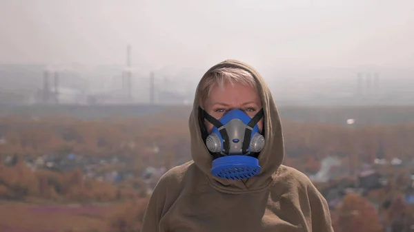 Eine Frau mit Atemschutzmaske steht vor dem Hintergrund rauchender Fabrikpfeifen — Stockfoto