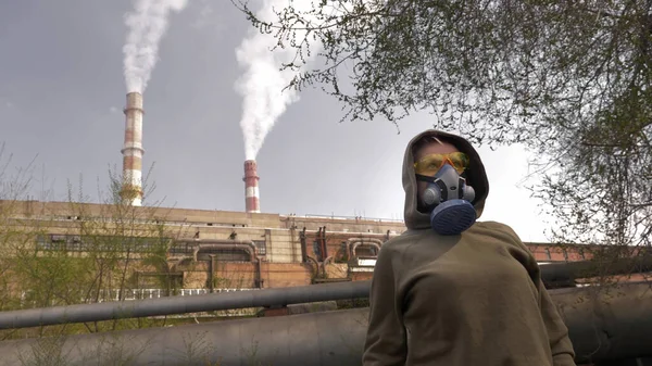 A woman in a respirator stands on the background of smoking factory pipes — Stock Photo, Image