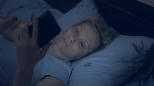Vrouw die lijdt aan slapeloosheid maakt gebruik van een smartphone terwijl liggend in bed in het donker — Stockfoto