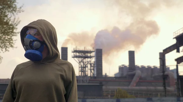 A woman in a respirator stands on the background of smoking factory pipes — Stock Photo, Image