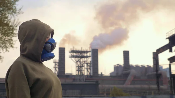 Eine Frau mit Atemschutzmaske steht vor dem Hintergrund rauchender Fabrikpfeifen — Stockfoto