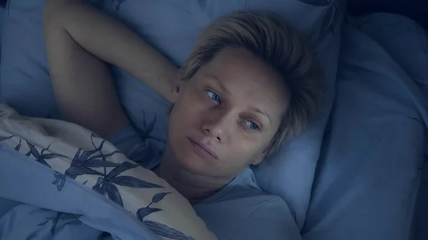 Женщина, страдающая шизофренией, лежит в кровати в темноте с открытыми глазами . — стоковое фото