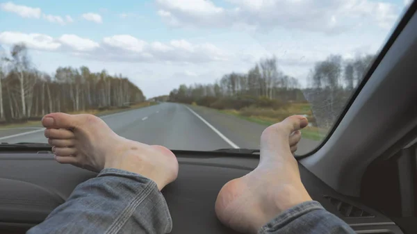 male bare feet on the dashboard of a moving car. traffic on the motorway