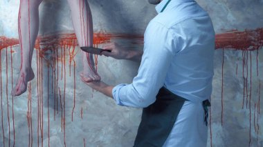 Arka planda kanlı duvarlar ve sallanan bacakları olan bir adam.