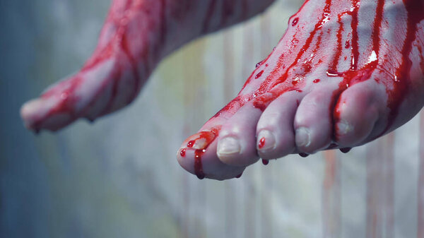 Крупный план. окровавленные ноги человека, висящего на фоне окровавленной стены
