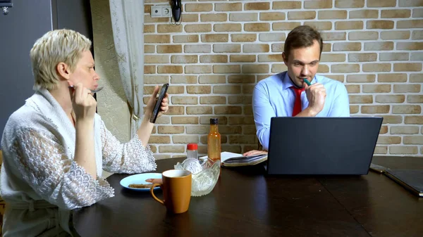 Ein Mann arbeitet zu Hause am Laptop in der Küche, Frau isst — Stockfoto