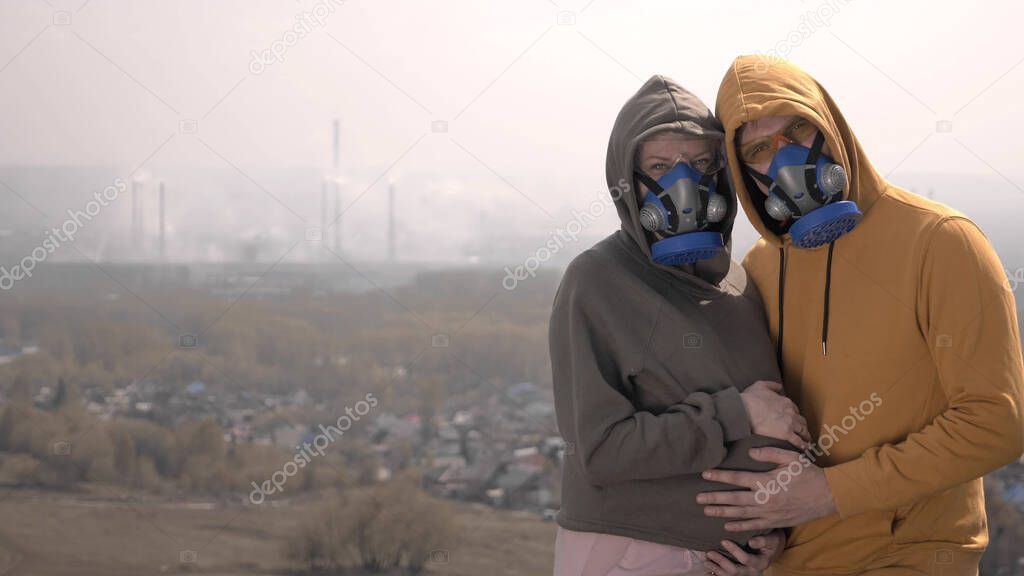 pregnant woman and her man in respirators on the street against factory pipes