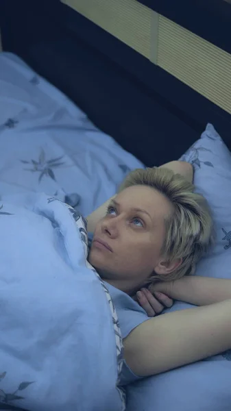 Vertical. una mujer que sufre de insomnio yace en la cama en la oscuridad —  Fotos de Stock