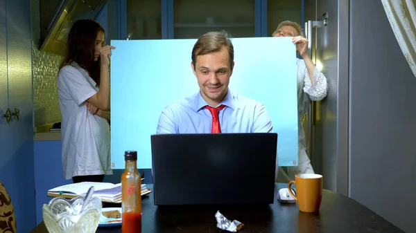 Un uomo tiene una videoconferenza a casa in cucina, sua moglie e sua figlia stanno tenendo uno sfondo — Foto Stock