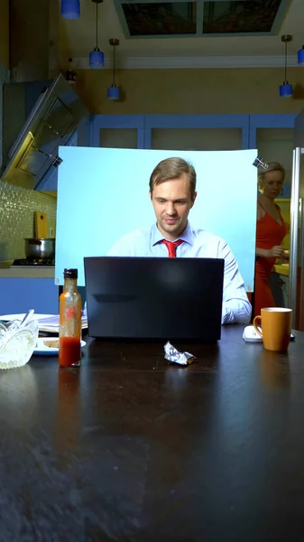 Verticalmente. Un hombre tiene una videoconferencia en casa en la cocina, su esposa mira en el refrigerador — Foto de Stock