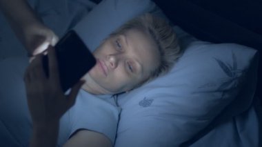 Uykusuzluk çeken kadın karanlıkta yatarken akıllı telefon kullanıyor.