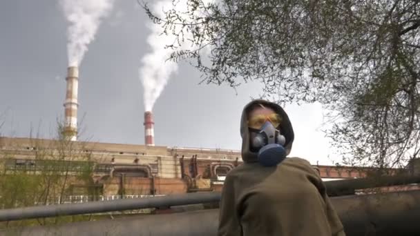 Una mujer en un respirador se para en el fondo de las pipas de la fábrica de fumar — Vídeo de stock