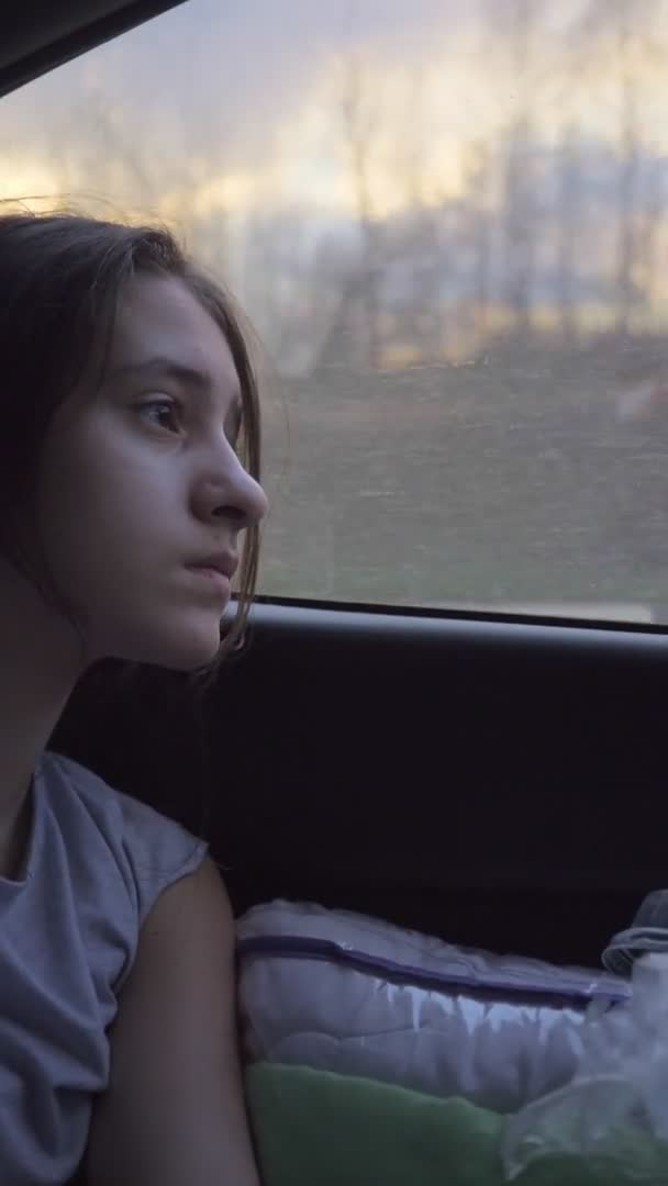 Κάθετα, κουρασμένος το κορίτσι κοιτάζει έξω από το παράθυρο ενός κινούμενου αυτοκινήτου. ταξίδι με αυτοκίνητο — Αρχείο Βίντεο