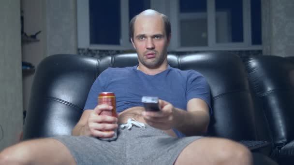 Lonely balding man at home in a chair with a beer and a remote control. — Stock Video