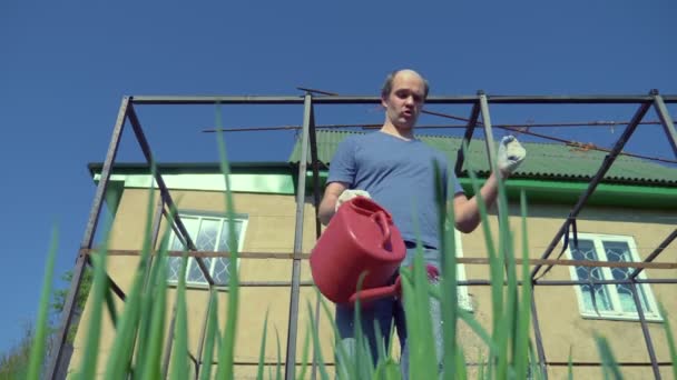 Kale man met een snor die vrolijk de tuin besproeit met een rode gieter — Stockvideo