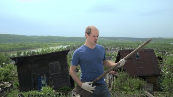 Rolig skallig man imiterar att spela gitarr med en spade på en gård — Stockvideo