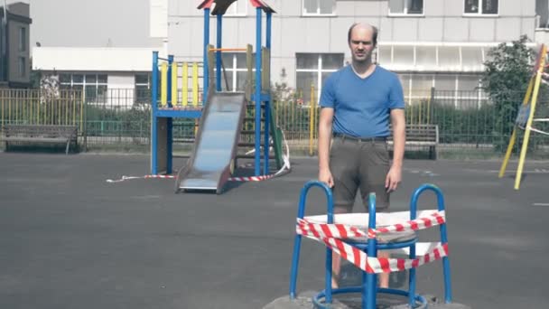 Vreemde kale kinderlijke man staat op een lege ingesloten de Speeltuin — Stockvideo