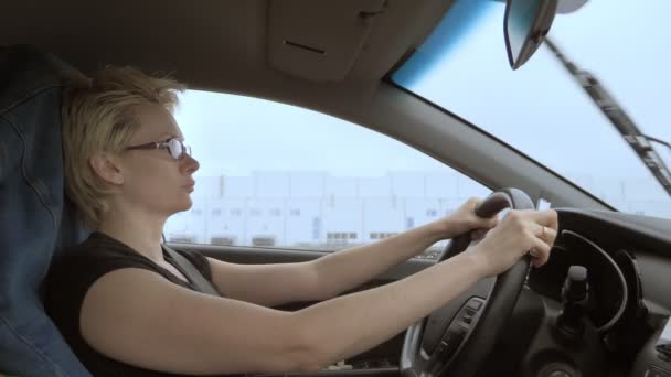 Mujer con corte de pelo corto con gafas conduciendo coche bajo la lluvia — Vídeos de Stock