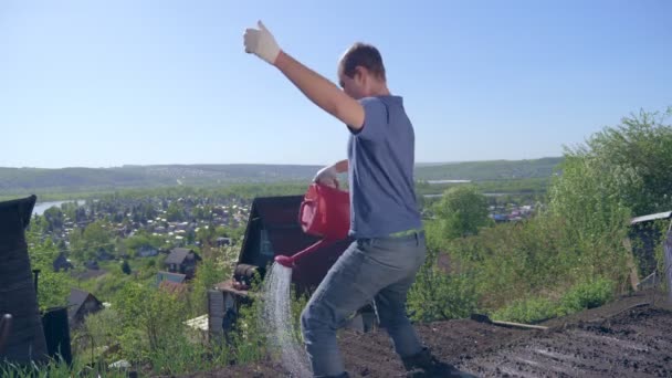 Glatzkopf mit Schnurrbart begießt freudig den Garten mit roter Gießkanne — Stockvideo