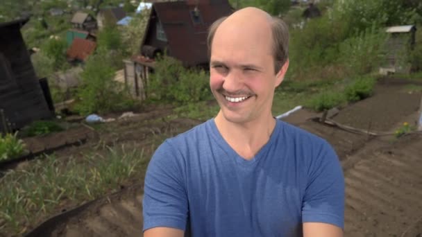 Portré, kopaszodó fiatal férfi vidéken nézi a kamerát, mosolyog — Stock videók