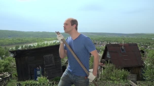 Lustiger Glatzkopf imitiert auf einem Bauernhof das Spielen einer Gitarre mit einer Schaufel — Stockvideo