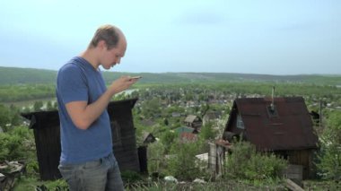 Yakışıklı adam dağdaki bahçede akıllı telefon kullanıyor.