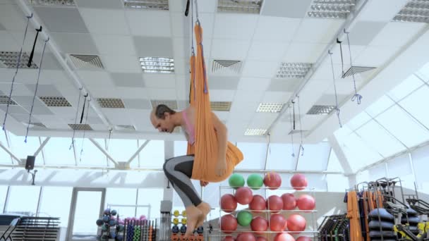 Calvo uomo su un'amaca per aero yoga guarda giù cercando di saltare — Video Stock