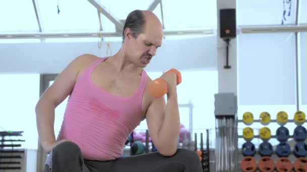 Medium shot. Bald funny man is training with dumbbells in the gym — Stock Video