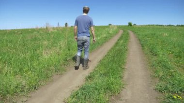 Dikiz aynası. Tarla yolunda yürüyen muşamba çizmeli kel köylü.