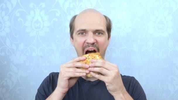 Retrato hambre bigote calvicie hombre muerde una hamburguesa — Vídeo de stock