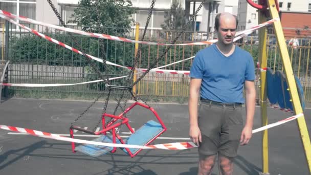 Vreemde kale kinderlijke man staat op een lege ingesloten de Speeltuin — Stockvideo