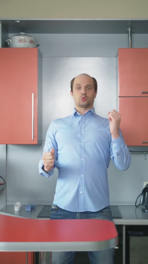 Вертикально. лысеющий мужчина в рубашке танцует дома на кухне — стоковое видео