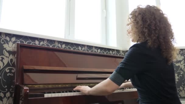 Bella ragazza in occhiali con i capelli ricci suona il pianoforte. vista laterale — Video Stock