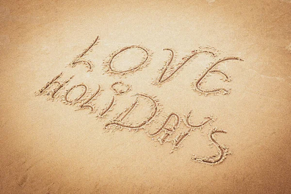 Handwritten inscription Love Holidays on the beach sand