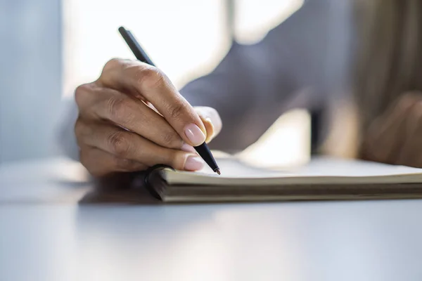 Fechar-se da escrita de mão de mulher em bloco de notas em uma mesa branca. Focado em uma mão com caneta — Fotografia de Stock